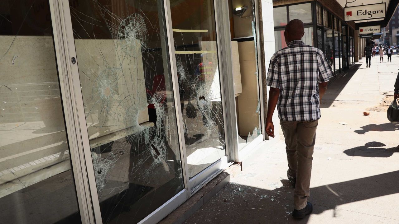 A man walks past smashed shop windows in Harare on Thursday.