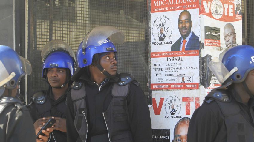 A Zimbabwean Riot policeman looks at the campaign poster of main opposition leader, Nelson Chamisa outside the party headquarters in Harare, Zimbabwe, Thursday, Aug, 2, 2018. Zimbabwe's acting President said Thursday that his government had been in touch with the main opposition leader in an attempt to ease tensions after election related violence in the capital. (AP Photo/Tsvangirayi Mukwazhi)
