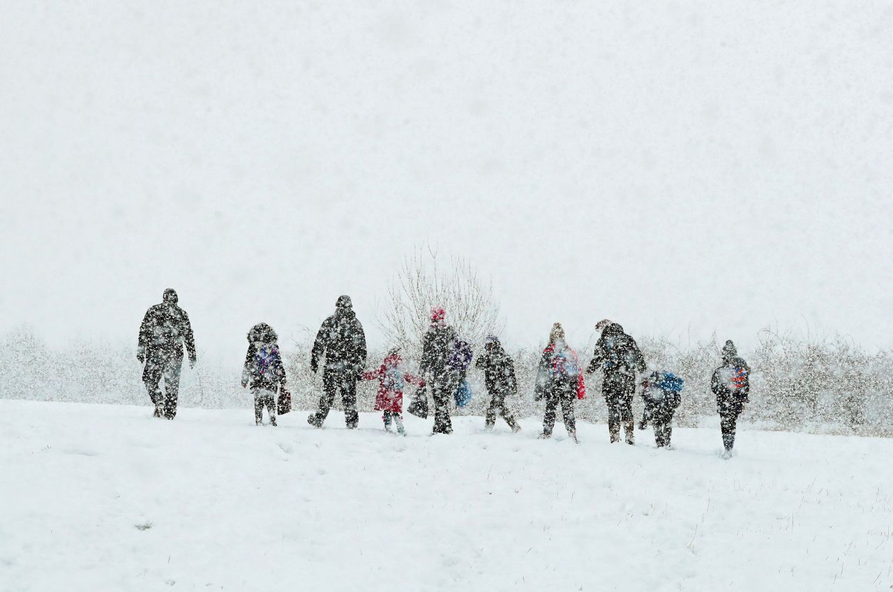 As heavy snow falls, parents walk their children to school in Ashford, a town in the county of Kent, England.