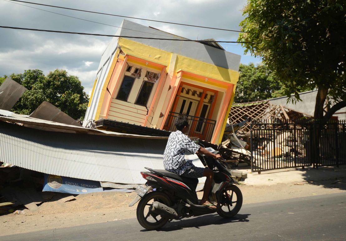 A man rides a motorcycle past a damaged house in northern Lombok on Tuesday.
