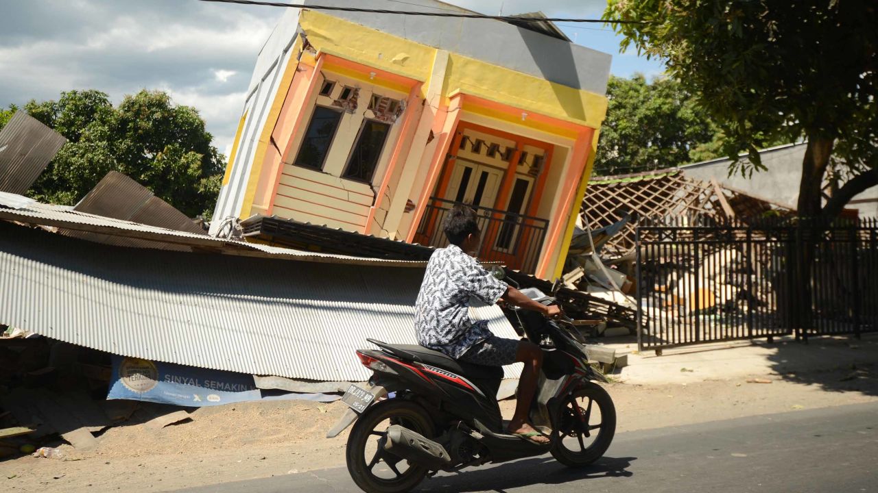 A man rides a motorcycle past a damaged house in northern Lombok on Tuesday.