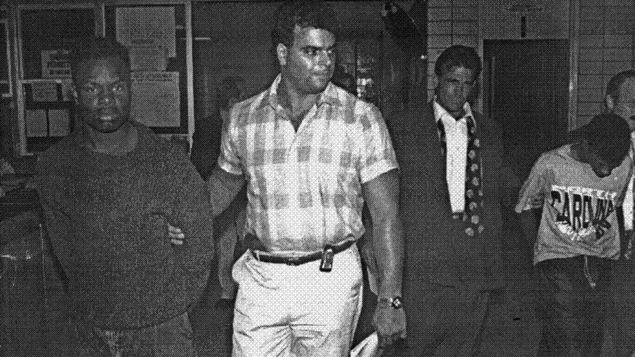 John Bunn, 14, right, and Rosean Hargrove, 17, arrested at the 77th Precinct in Brooklyn in August 1991. NYPD Detective Louis Scarcella (open jacket and loose tie) holds Bunn.