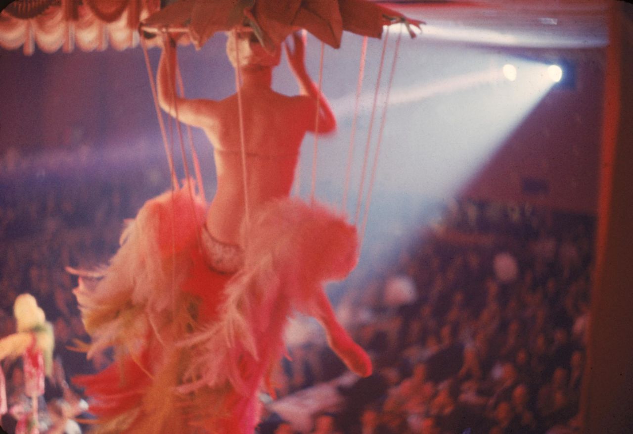 A costumed showgirl sits on a swing above the audience during a performance at the Latin Quarter nightclub, New York, New York, 1958.