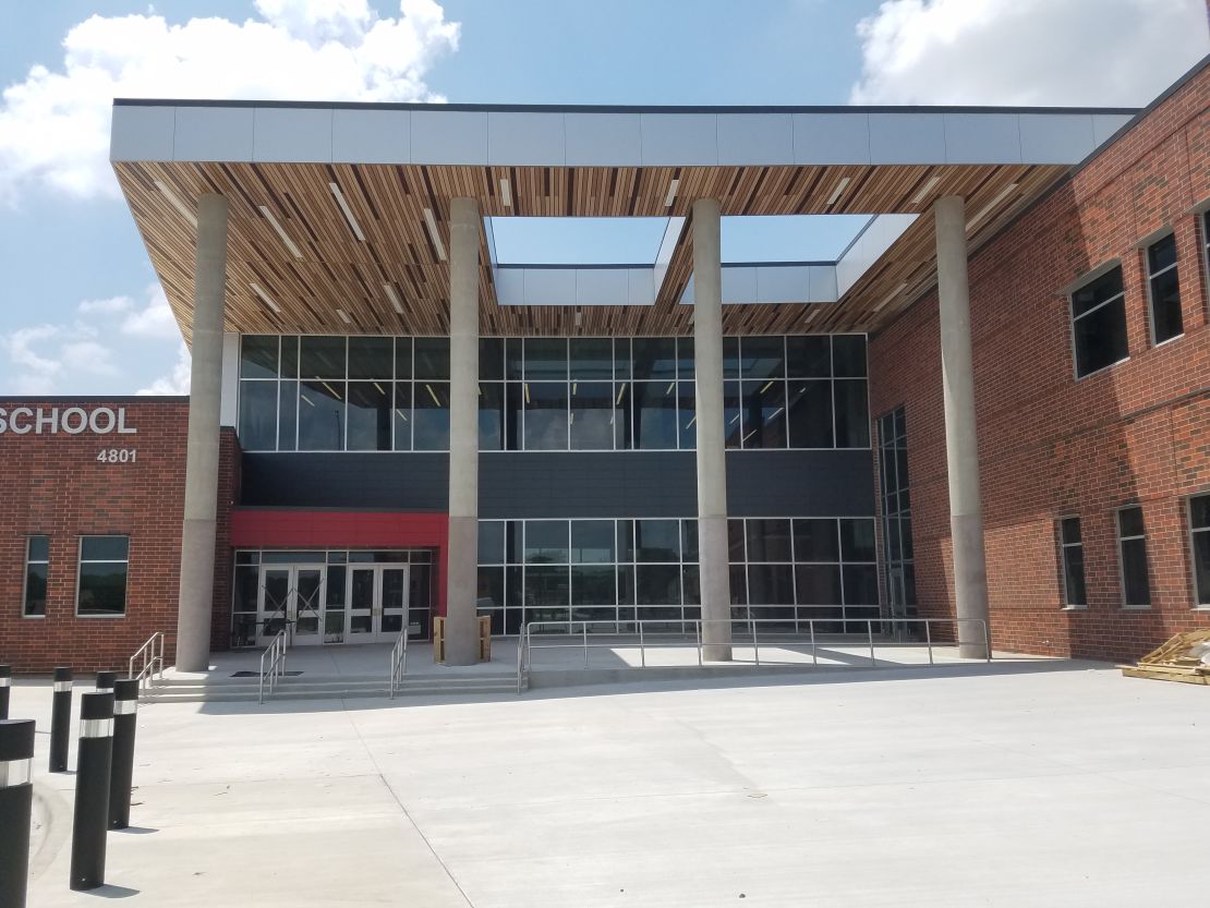 The entrance to this middle school, designed by PBK/IN2 Architecture, includes large glass windows, protective poles and an entrance clearly outlined in red.