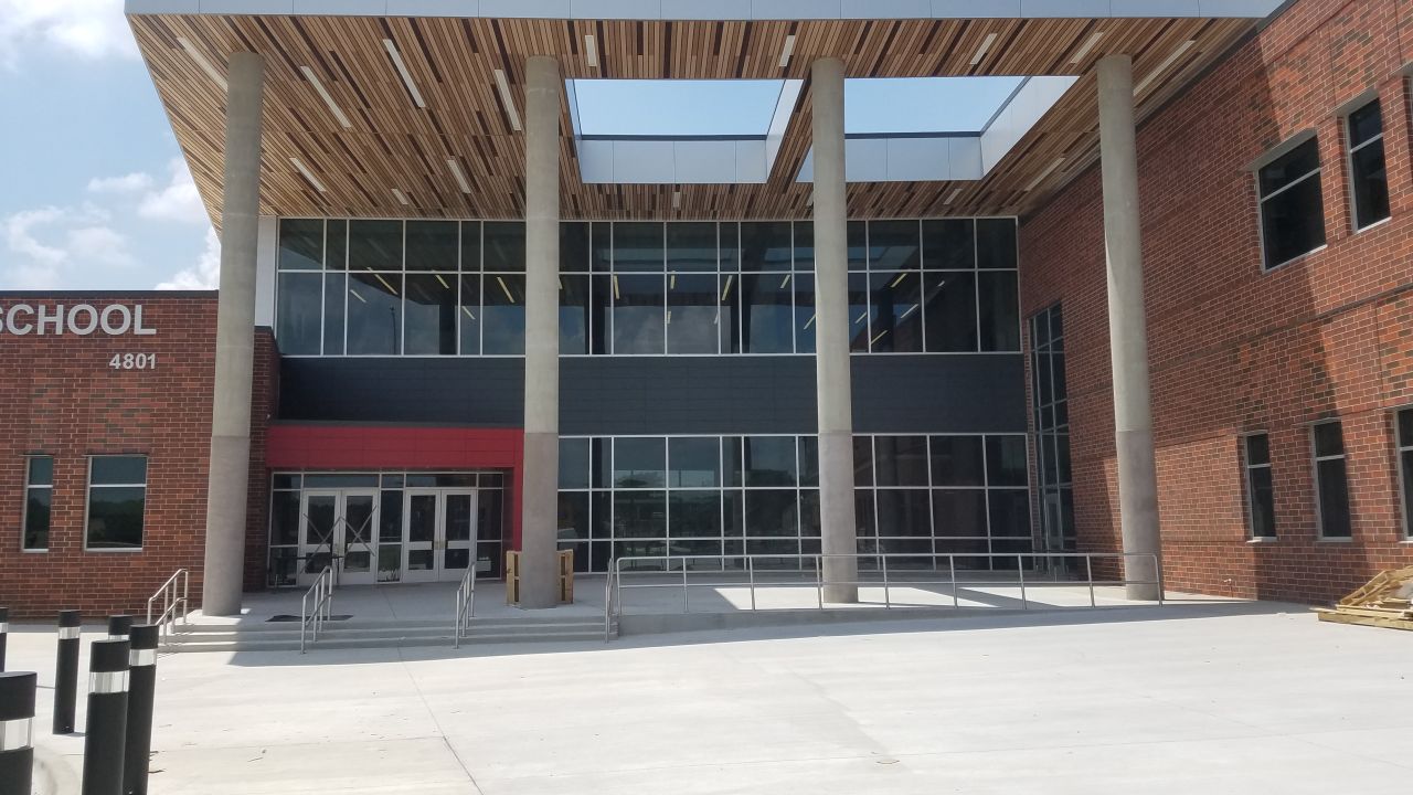 The entrance to this middle school, designed by PBK/IN2 Architecture, includes large glass windows, protective poles and an entrance clearly outlined in red.