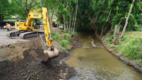 Workers clean debris from a stream near Honolulu, trying to get ahead of water from the hurricane.