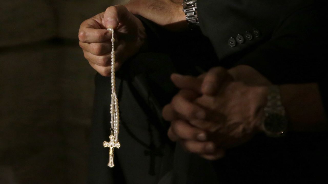 FILE- In this Sept. 24, 2015, file photo a member of the clergy prays the rosary as he waits for Pope Francis to arrive at St. Patrick's Cathedral for evening prayer service in New York. Across the U.S., Catholics once faithful with their financial support to their churches are searching for ways to respond to the constant sex-abuse scandals that have tarnished the institution in which they believe, with back-to-back scandals in the past two months. (AP Photo/Mary Altaffer, File)