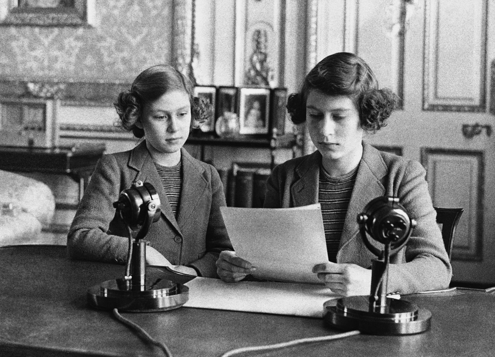 A 14-year-old Elizabeth, right, sits next to her sister for a radio broadcast on October 13, 1940. On the broadcast, her first, she said that England's children were full of cheerfulness and courage.