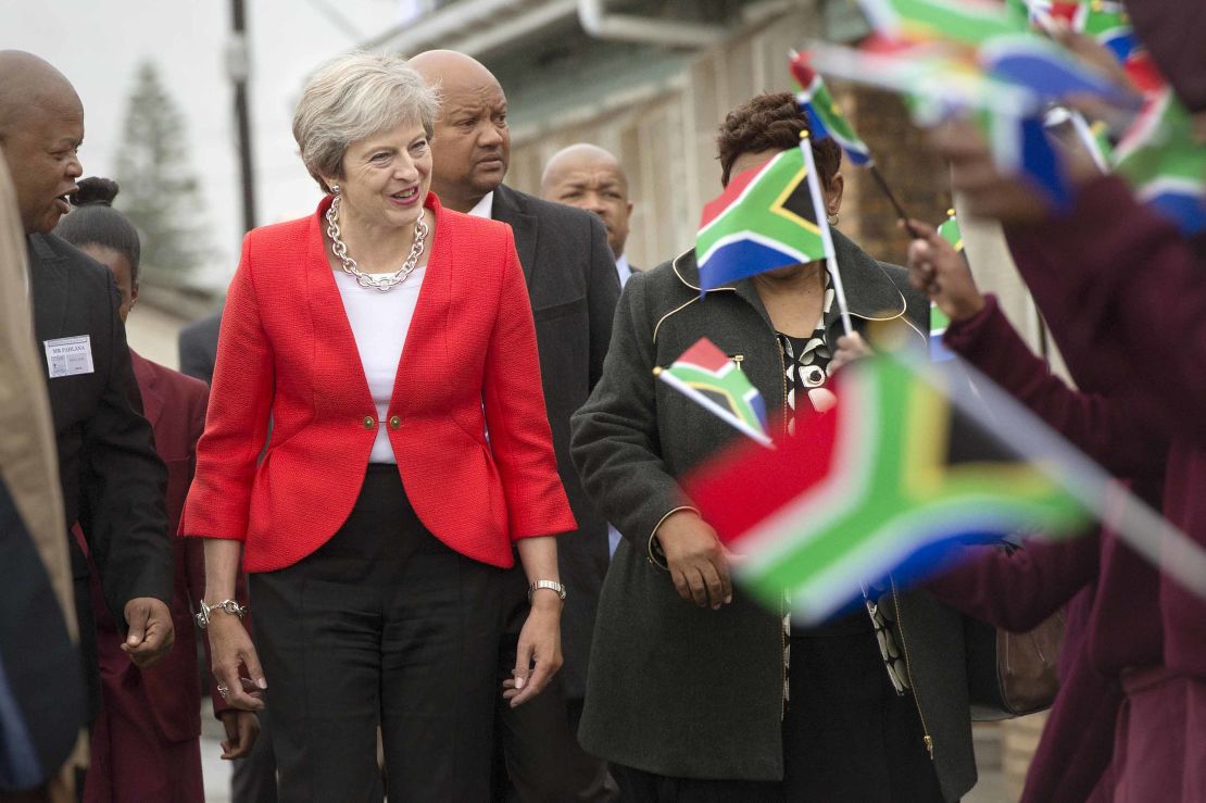 Britain's Prime Minister Theresa May (L) is greeted by schoolchildren waving British and South African flags.