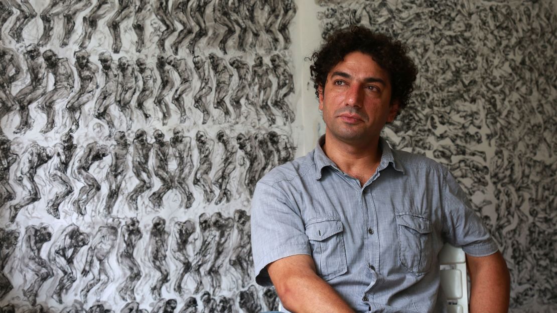 Syrian artist and painter Najah al-Bukai sits in front of his drawings which he used to document torture and the dead at Syrian prisons.