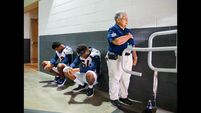 A stadium security guard stands with her hand over her heart as Denver Broncos linebacker Brandon Marshall and wide receiver Demaryius Thomas sit in silent protest during the national anthem before playing the Arizona Cardinals on Friday, August 31.