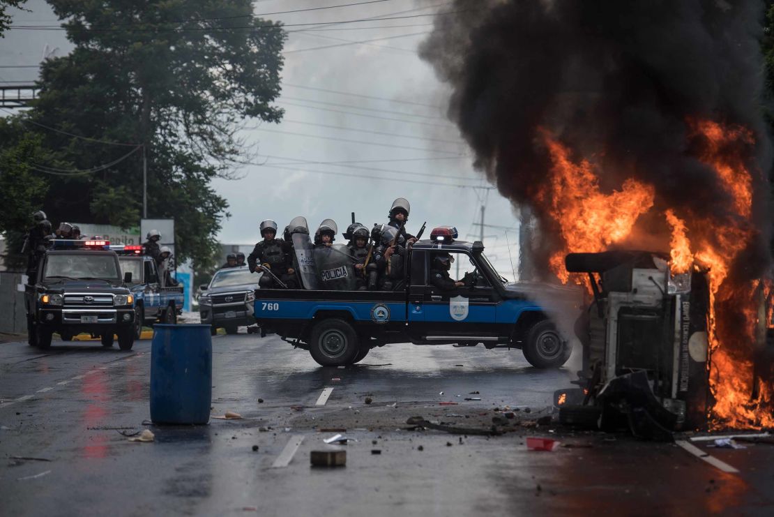 Heavily armed police officers sit on a pick-up and stand next to a burning police car in Managua on September 2, 2018.