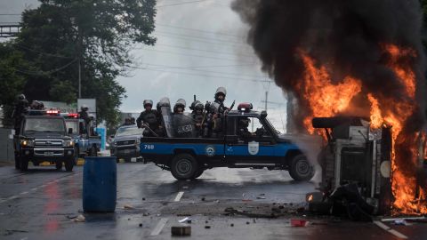 Heavily armed police officers sit on a pick-up and stand next to a burning police car in Managua on September 2, 2018.