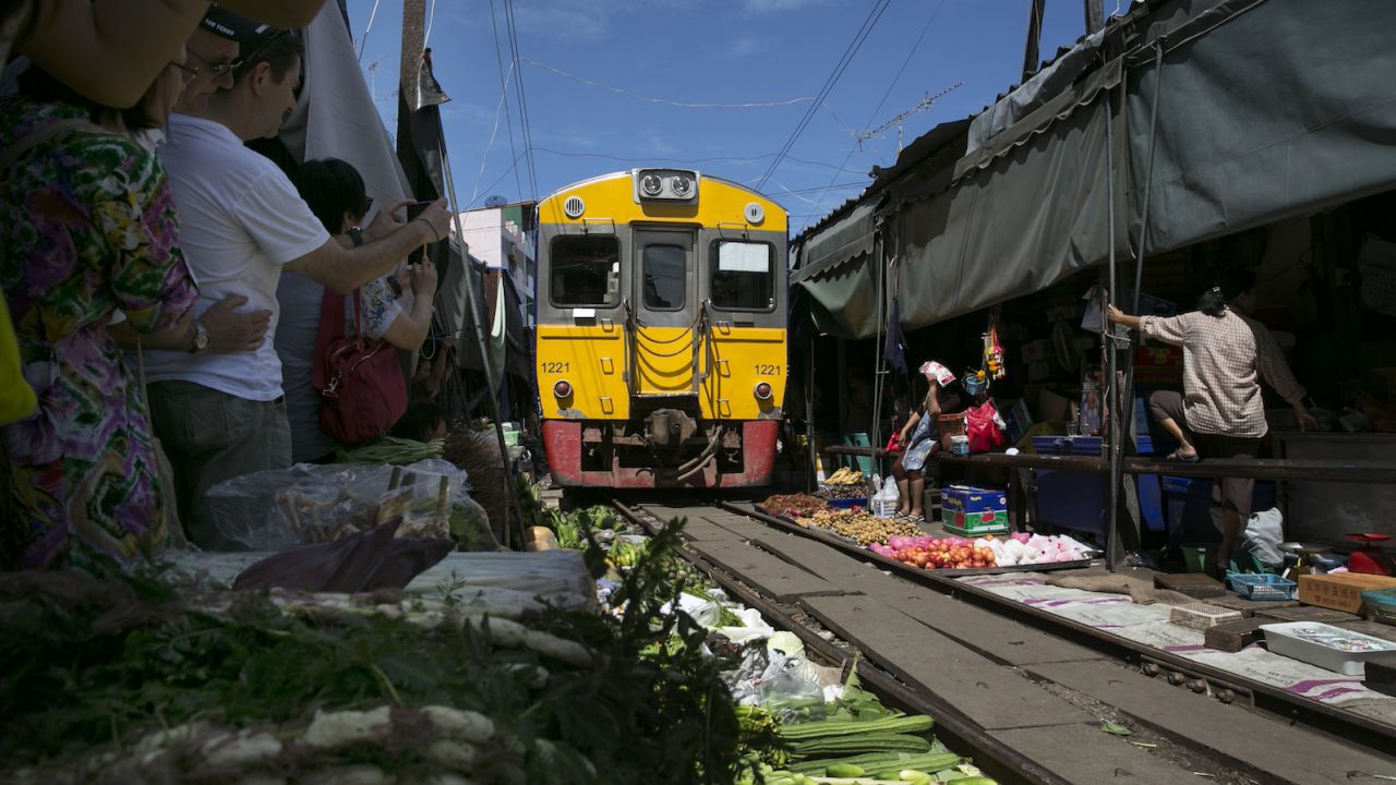 A train passes through the Folding Umbrella Market. Notice how close those veggies are to the tracks.