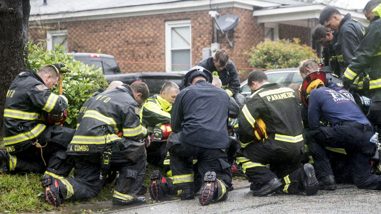 Emergency responders pray in front of a home after removing bodies that had been trapped by a fallen tree.