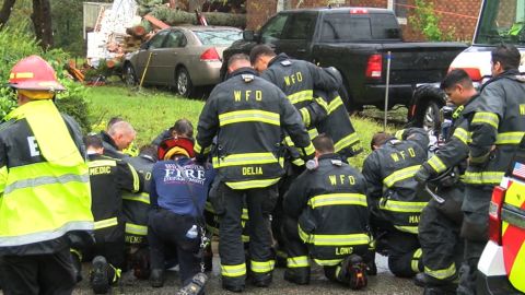 Firefighters pray at the home where a woman and her child were killed by a falling tree on Friday.