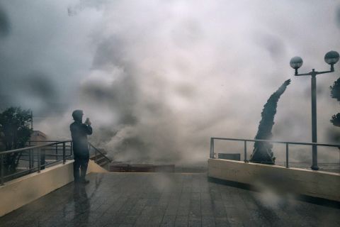 A man takes a photograph as waves crash over a promenade in Hong Kong, on Sunday.