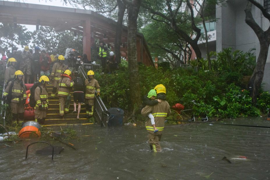 A fire rescue worker helps a child cross a flooded street in the village of Lei Yu Mun in Hong Kong.