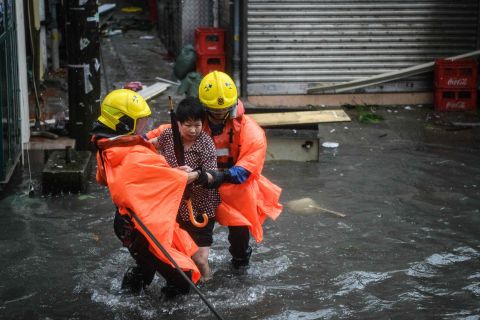 Rescue workers help a woman to cross a flooded street in the village of Lei Yu Mun, in Hong Kong on Sunday.