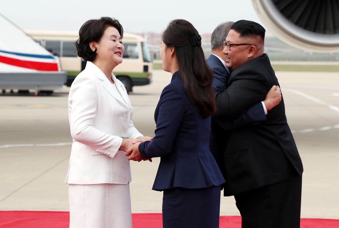 Moon Jae-in and Kim Jong Un hug as their wives shake hands.