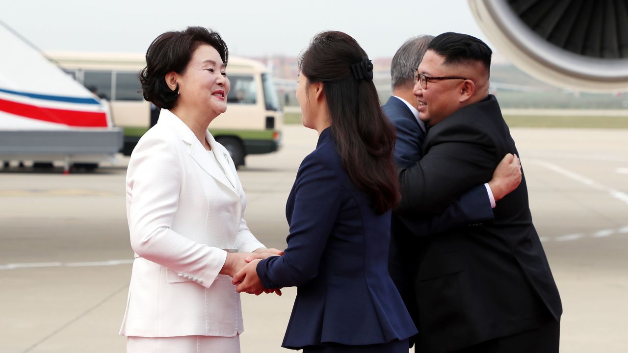 Moon Jae-in and Kim Jong Un hug as their wives shake hands.
