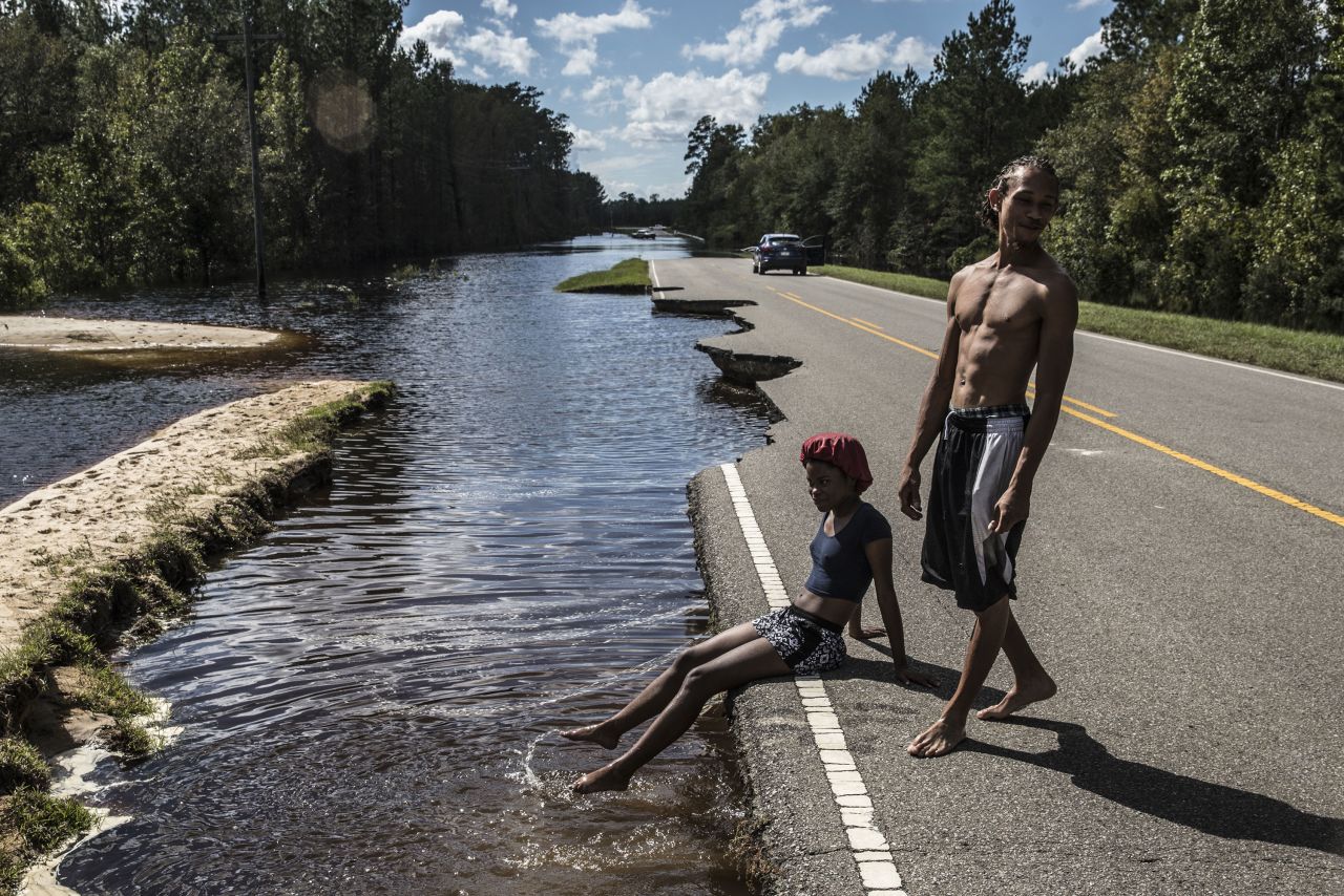 A woman in Currie, North Carolina, sits on a damaged road surrounded by floodwaters on Tuesday, September 18.