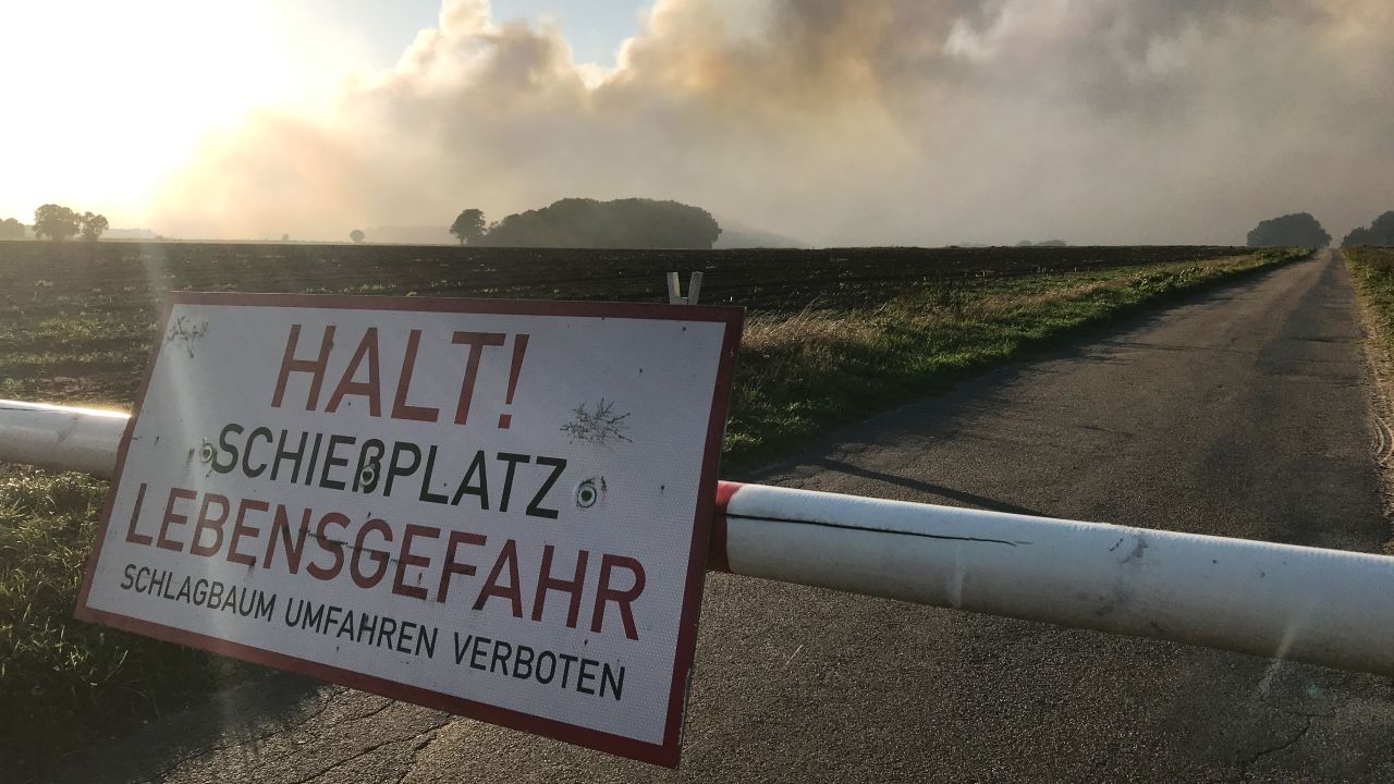 A sign reads, "Stop! Artillery range, danger to life" as smoke from the moor fire rises into the sky.