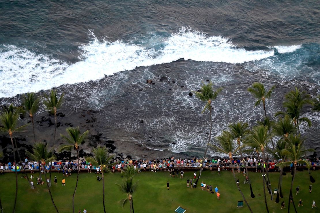 Spectators sit on a rock wall during the Ironman World Championship on October 14, 2017.