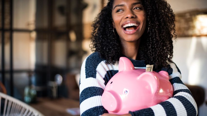 Black young woman hugging her pink piggy bank