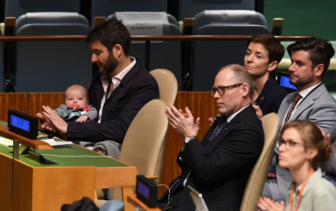 Clarke Gayford (C) claps while holding his daughter Neve, as his wife Jacinda Ardern, Prime Minister of New Zealand, speaks during the Nelson Mandela Peace Summit in the United Nations assembly hall in New York. 