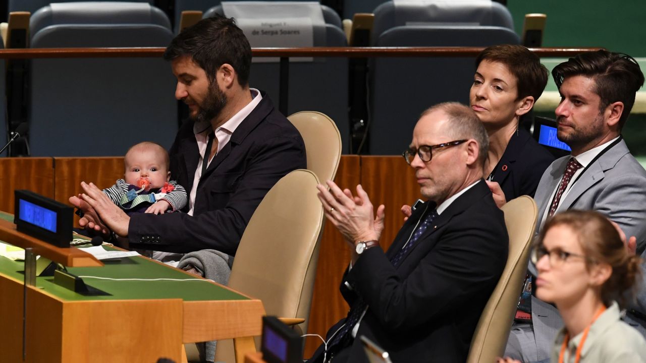 Clarke Gayford (C) claps while holding his daughter Neve, as his wife Jacinda Ardern, Prime Minister of New Zealand, speaks during the Nelson Mandela Peace Summit in the United Nations assembly hall in New York. 