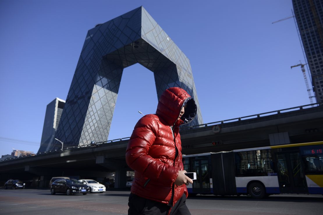 A man walks down the street as the iconic CCTV headquarters loom in the background in the central business district of Beijing on January 20, 2017.