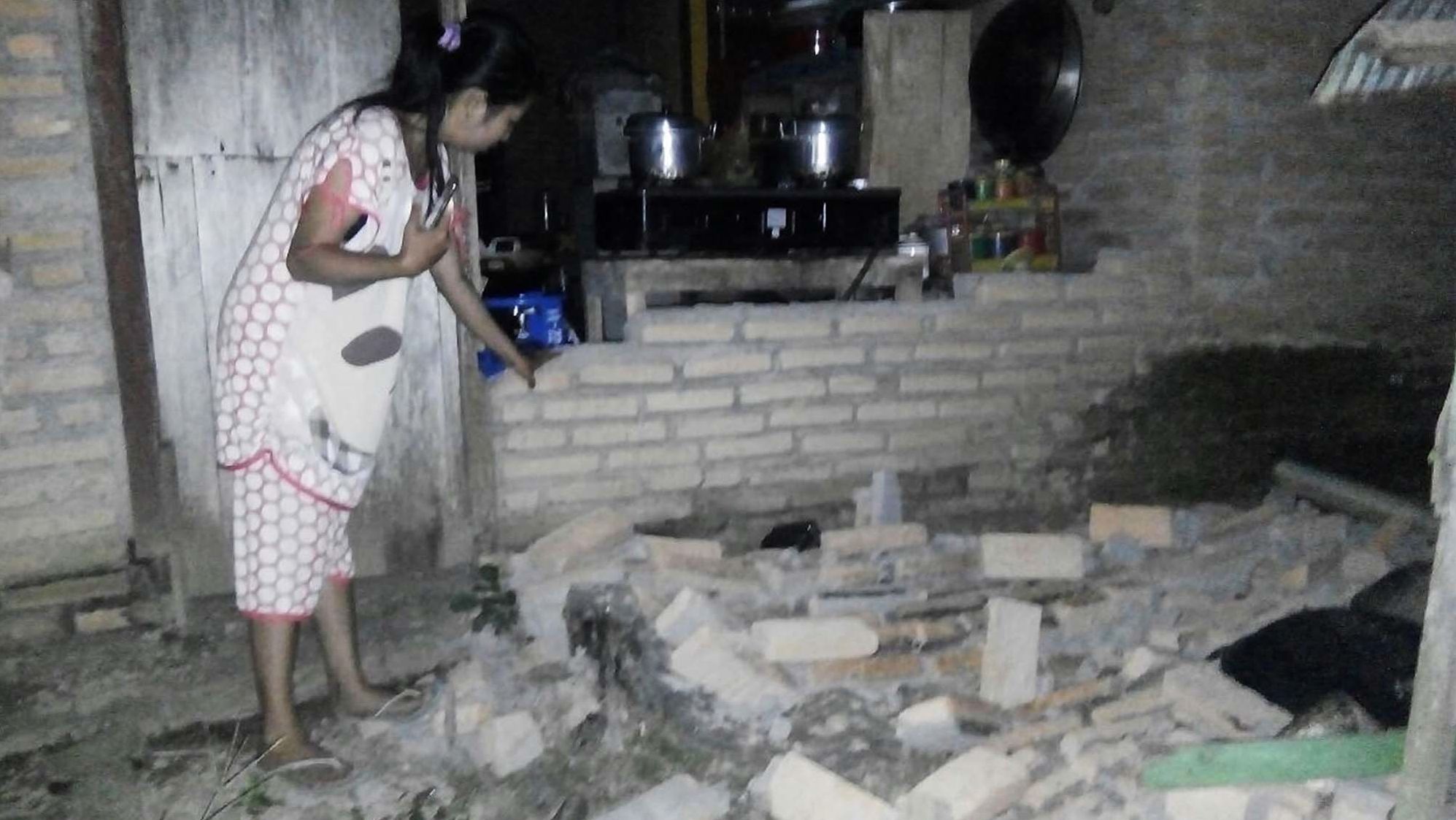 A resident is seen beside the collapsed brick wall of her house at Tobadak village in Central Mamuju, western Sulawesi province, on September 28 after a strong earthquake hit the area.