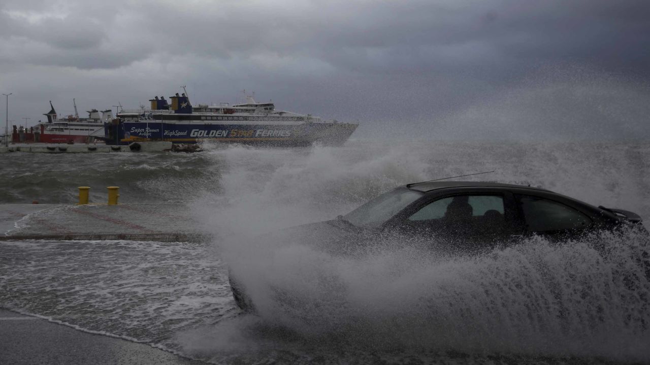 A car drives through seawater from crashing waves on the road during bad weather at the port of Rafina, east of Athens, on Thursday, Sept. 27