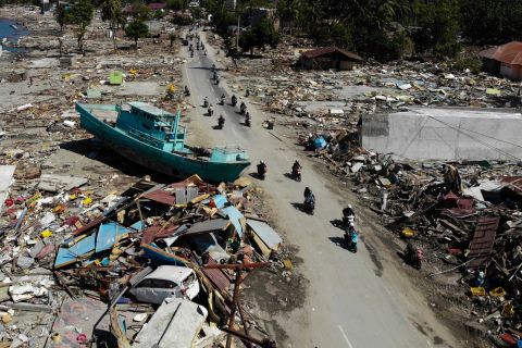 People ride past a boat and other debris in Palu on October 1.