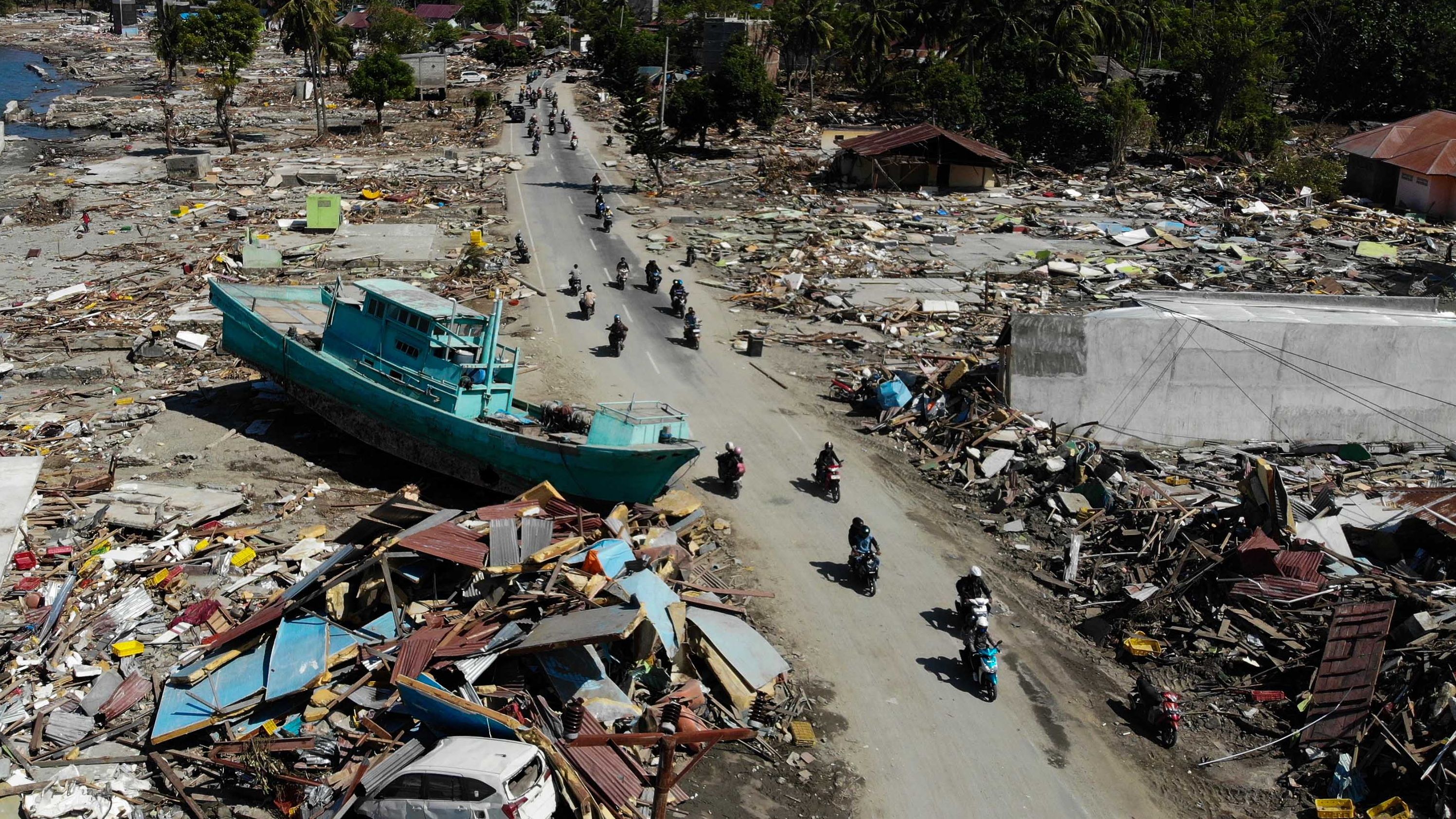 People ride past a boat and other debris in Palu on October 1.