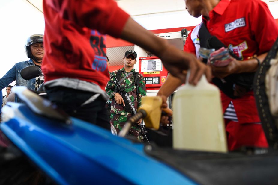 An Indonesian soldier stands guard at a service station as people line up to fill gasoline containers on October 1.