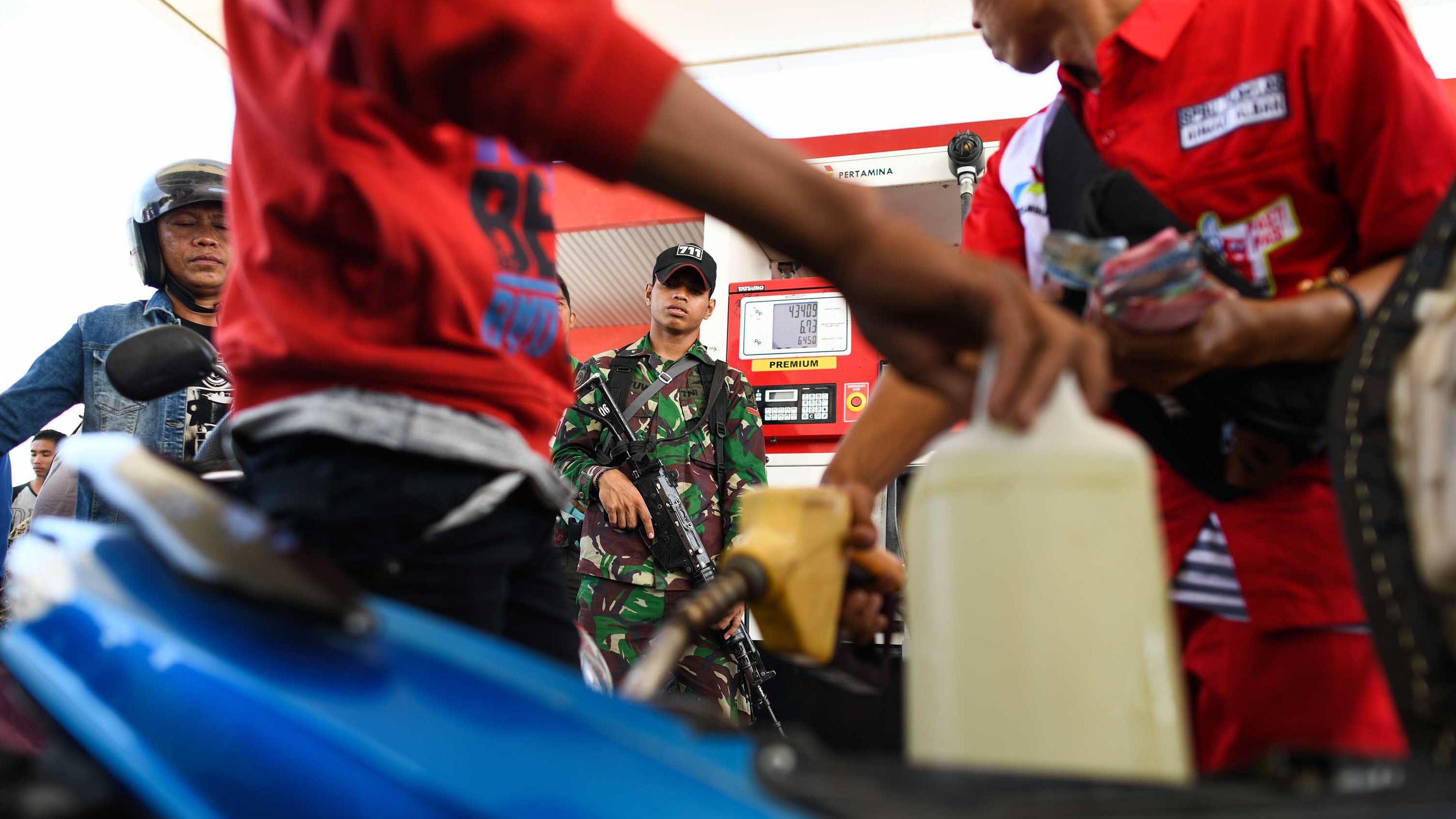 An Indonesian soldier stands guard at a service station as people line up to fill gasoline containers on October 1.