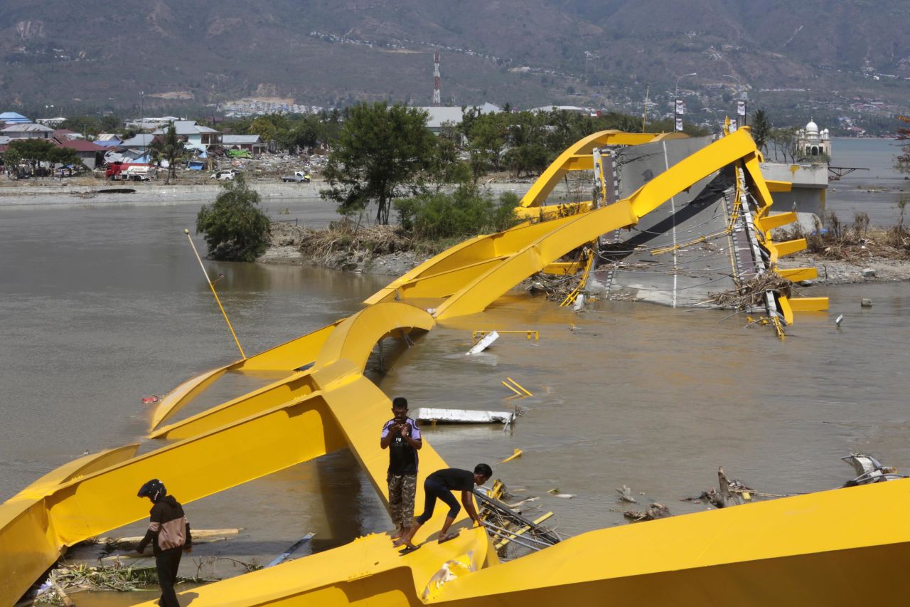 People survey the wreckage of a bridge near Talise Beach in Palu.
