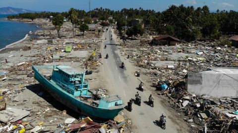 TOPSHOT - People drive past a washed up boat and collapsed buildings in Palu on October 1, 2018, after an earthquake and tsunami hit the area on September 28. - Mass graves were being readied on October 1 for hundreds of victims of the Indonesian quake and tsunami as authorities battled to stave off disease and reach desperate people still trapped under shattered buildings. (Photo by JEWEL SAMAD / AFP)        (Photo credit should read JEWEL SAMAD/AFP/Getty Images)