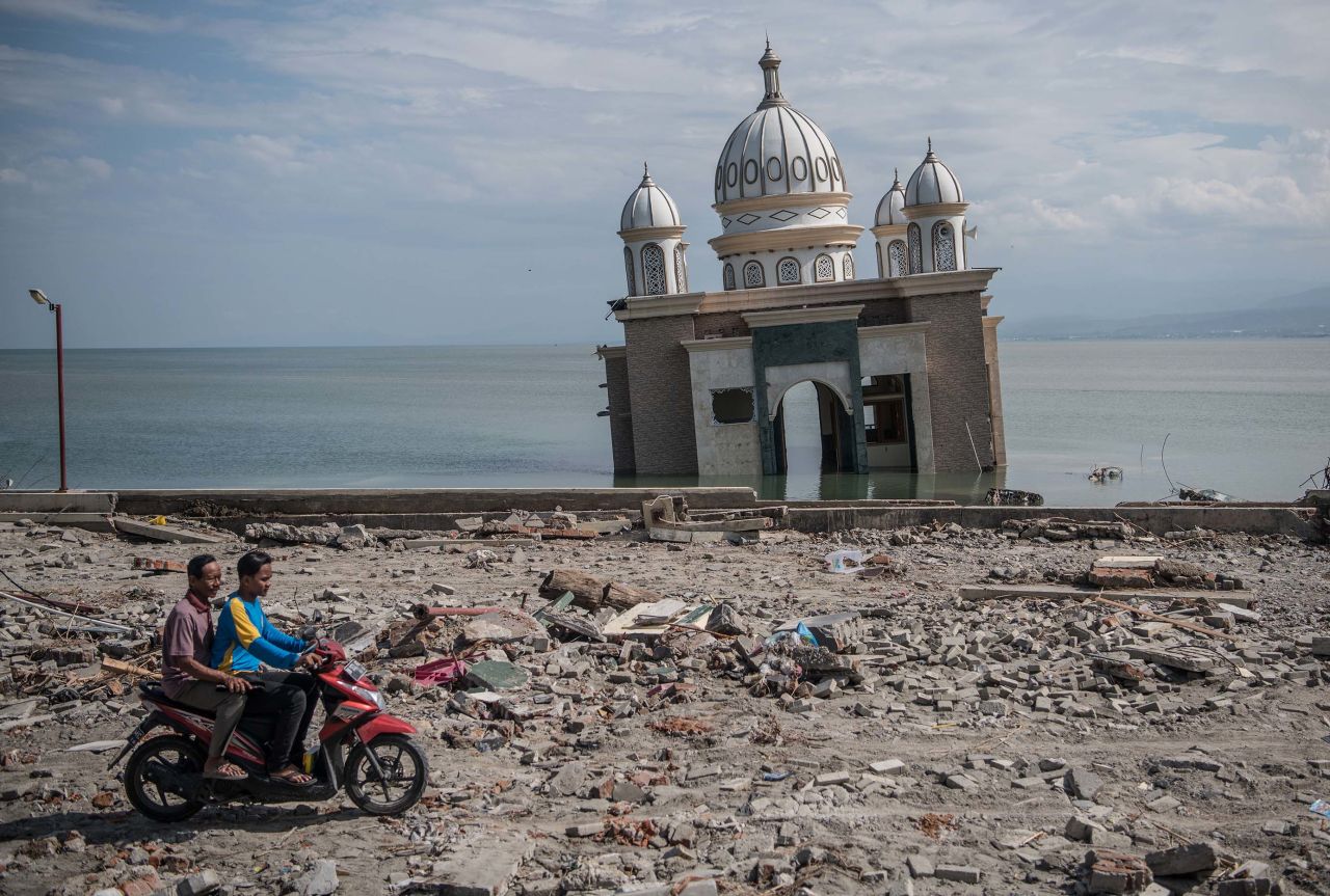 People ride a scooter past a partially submerged mosque in Palu on October 2. The mosque was knocked from its foundation during the quake and tsunami.