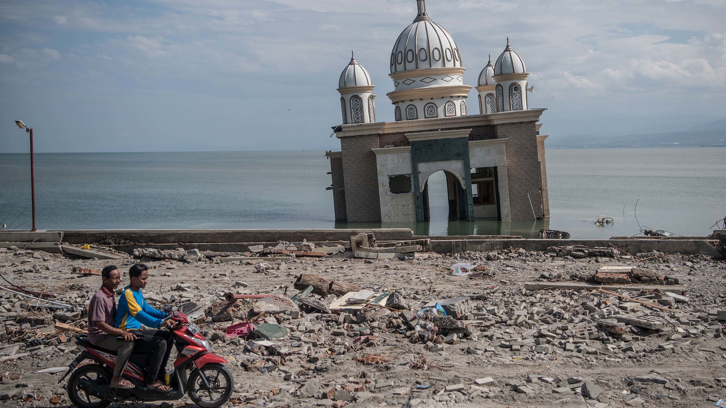People ride a scooter past a partially submerged mosque in Palu on October 2. The mosque was knocked from its foundation during the quake and tsunami.