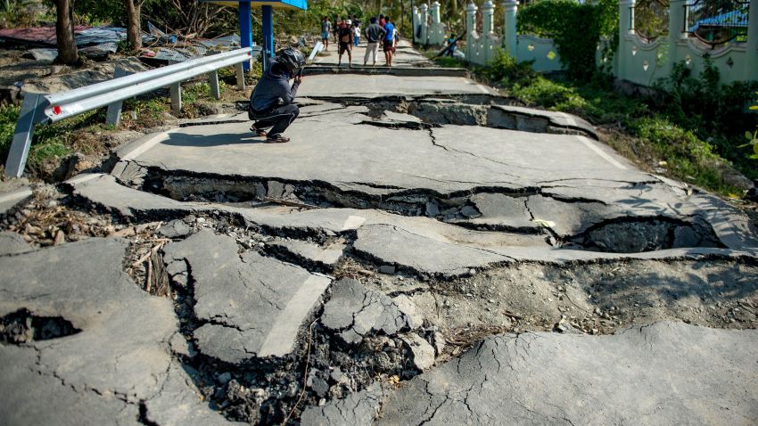 A motorcyclist takes photos of a damaged road in Petobo village in Palu, Indonesia's Central Sulawesi on October 1, 2018, after an earthquake and tsunami hit the area on September 28. - Indonesian volunteers began burying bodies in a mass grave with space for more than a thousand people on October 1, victims of a quake-tsunami that devastated swathes of Sulawesi and left authorities struggling to deal with the sheer scale of the disaster. (Photo by Bay ISMOYO / AFP)        (Photo credit should read BAY ISMOYO/AFP/Getty Images)