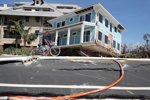 Tom Bailey walks his bike past a home that was carried across a road and slammed up against a condo complex in Mexico Beach. 
