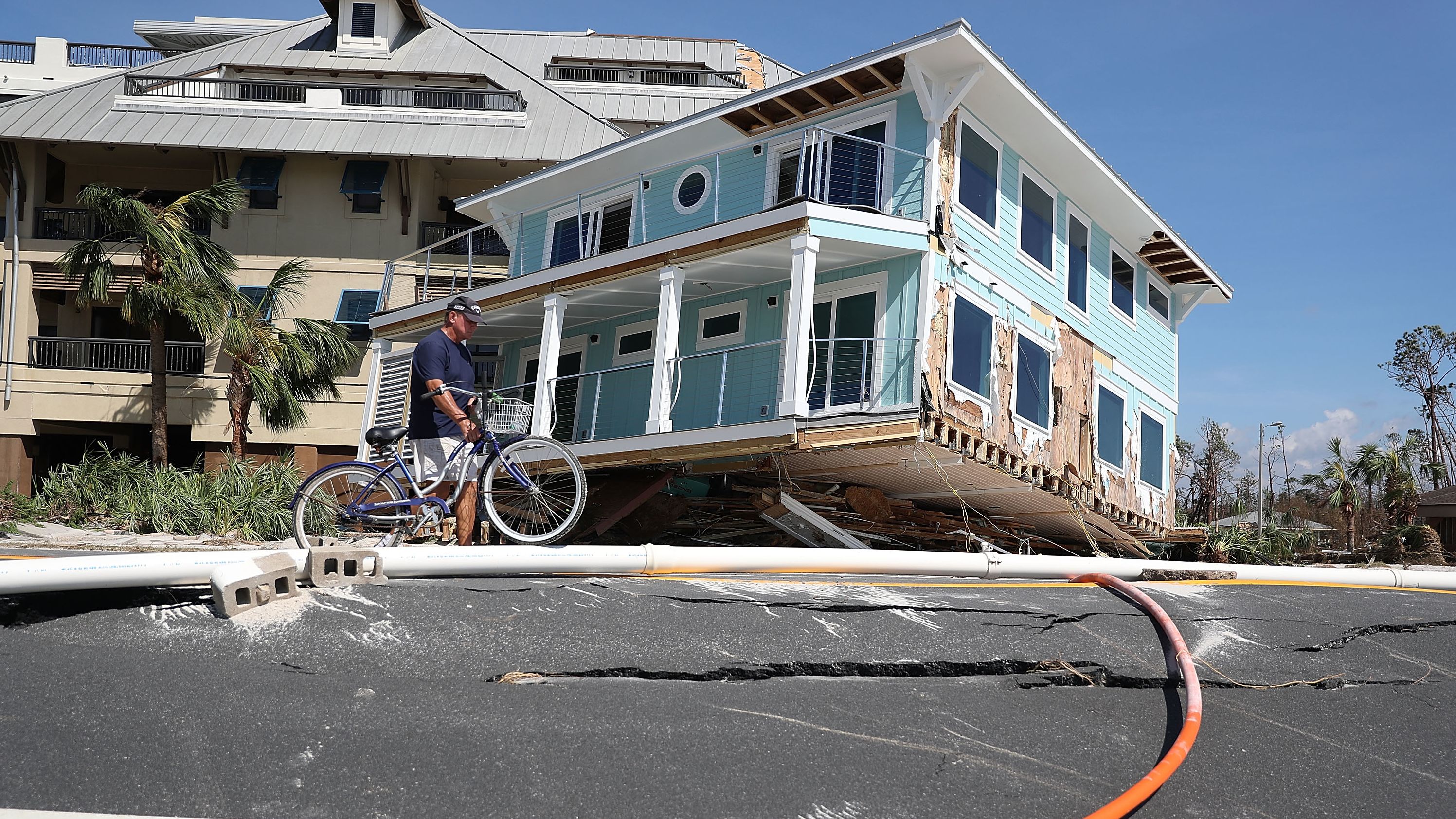 Tom Bailey walks his bike past a home that was carried across a road and slammed up against a condo complex in Mexico Beach. 