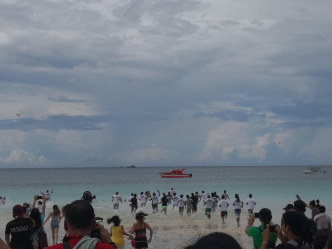 Tourists taking part in Boracay's limited-access soft opening run into the water following the island's six-month cleanup.