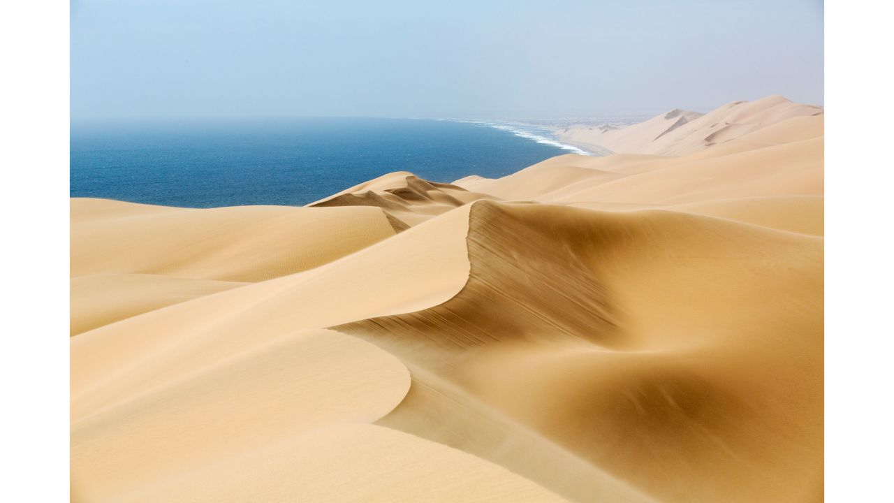 Category: Earth's Environments.
A high dune on Namibia's desert coastline, where mounds of wind-sculpted sand merge with the Atlantic Ocean.