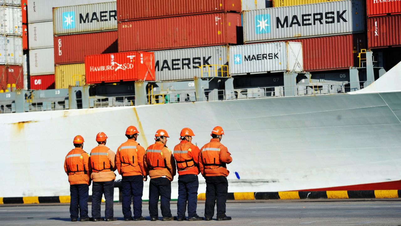 This photo taken on April 8, 2018 shows workers stand in line next to a container ship at a port in Qingdao in China's eastern Shandong province.