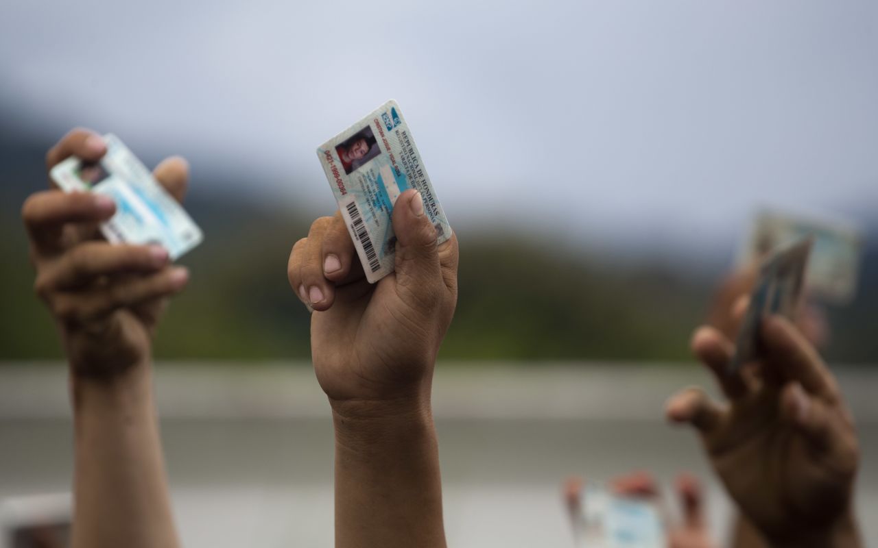 Honduran migrants holds up their national ID cards as Guatemalan police block them and their caravan after the group crossed the Honduras-Guatemala border in Esquipulas, Guatemala, on Monday, October 15, 2018. Police stopped the migrants for several hours but the travelers refused to return to the border and were eventually allowed to pass.  