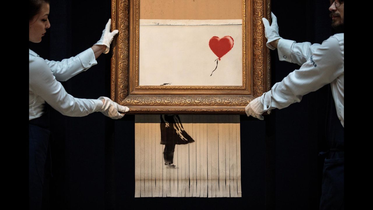 Sotheby's employees pose with "Love is in the Bin" by British artist Banksy during a media preview at Sotheby's auction house in London on Friday, October 12. The work was renamed from "Girl with Balloon" after it <a href="https://www.cnn.com/style/article/banksy-painting-self-destructs-auction-trnd/index.html" target="_blank">shredded through the bottom of the frame as it was sold</a> during Sotheby's Contemporary Art Sale on October 5.